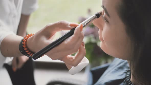 Hand of Makeup Artist Makes Makeup on Face of Beautiful Young Woman Using Makeup Brush