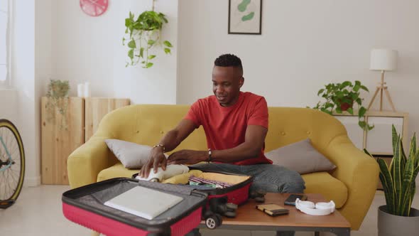 Young African Man Packing Clothes to Luggage Before Going on Summer Holidays