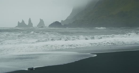 The Black Sand Beach of Reynisfjara with Waves Hitting the Shore on Foggy Rainy Stormy Day