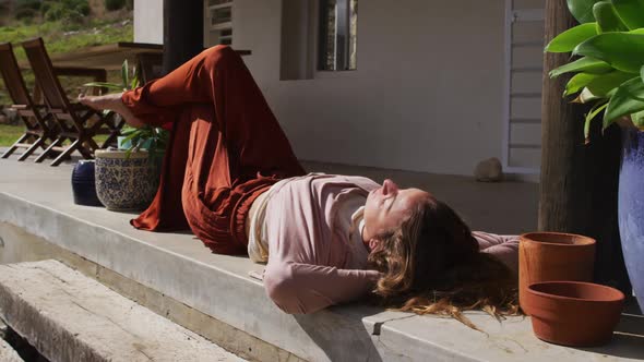 Happy caucasian woman lying in the sun, relaxing with eyes closed on cottage terrace