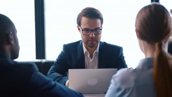 Businessman in suit talking in meeting with team using computer