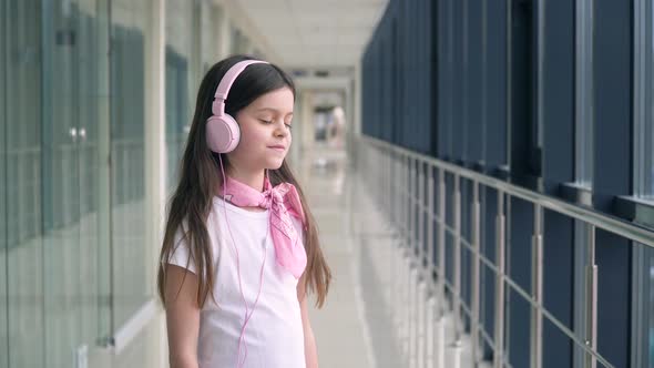 Little Girl Listens to Music in Pink Headphones at the Airport