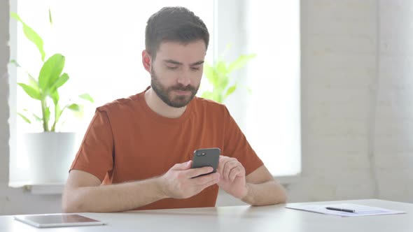 Young Man Browsing Internet on Smartphone in Office