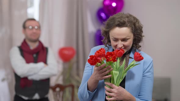 Excited Surprised Caucasian Wife Smelling Beautiful Red Tulips with Satisfied Facial Expression on