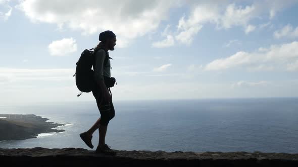 Male Hiker with Backpack Is Walking on the Edge of a Road in Canary Islands Above the Ocean