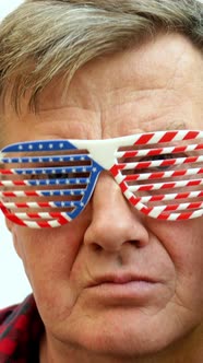 Serious Senior Mature Man Puts on Decorative Glasses in the Colors of the American Flag
