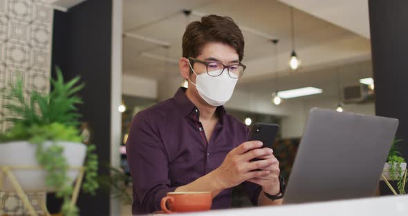 Asian man wearing face mask using smartphone while sitting at a cafe