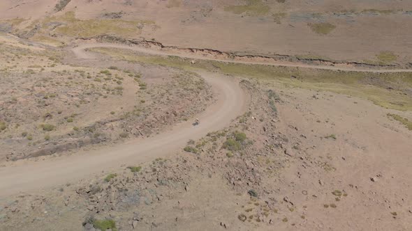 aerial shot following a mountain biker climbing up a pass on a gravel road