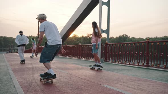 Group of Skaters Boys and Girls Ride Their Skateboards Across the Large City Bridge at Dawn