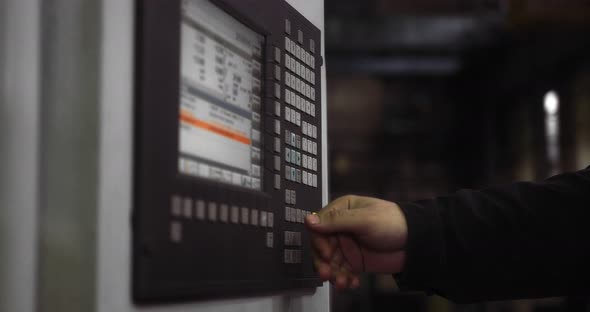 A Professional Working Man in a Helmet Stands Behind a CNC Machine