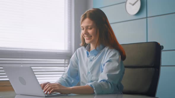 Professional medical worker brunette with long loose hair types on grey laptop