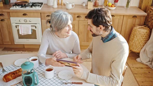 Top View of Happy Senior Lady Showing Family Photo in Frame to Her Adult Son Remembering Carefree