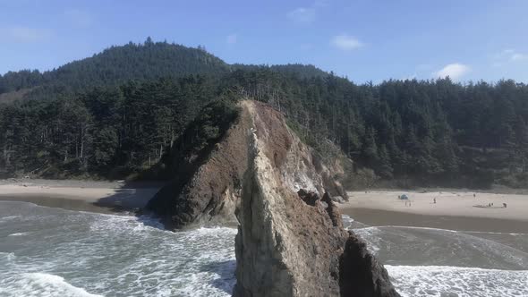 A lone seagull sits atop a large natural rock formation, Lion Rock, Arcadia Beach, aerial orbit