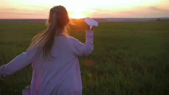 Happy Little Girl Playing with a Paper Airplane Outdoors During Sunset. Concept Big Child Dream.