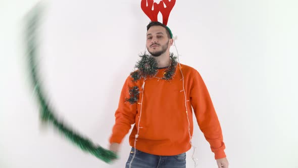 Young Happy Man Waving a Green Garland and Dancing. Man in Christmas Mood with Red Reindeer Antlers