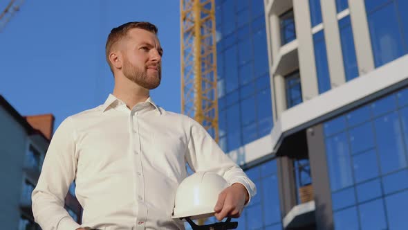 Architect Engineer in a White Shirt on the Background of a Modern Glass Building and Holding a