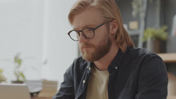 Young Man Working on Laptop and Looking at Camera in Office