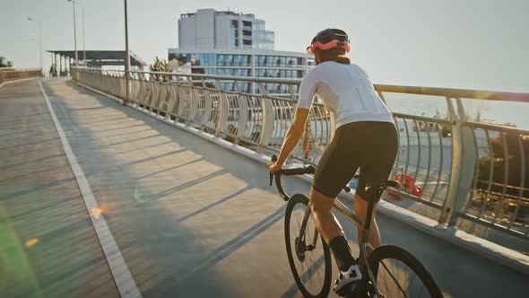 Woman in Protective Helmet is Riding Her Trekking Bike Uphill Along Bridge Nearby a Seacoast