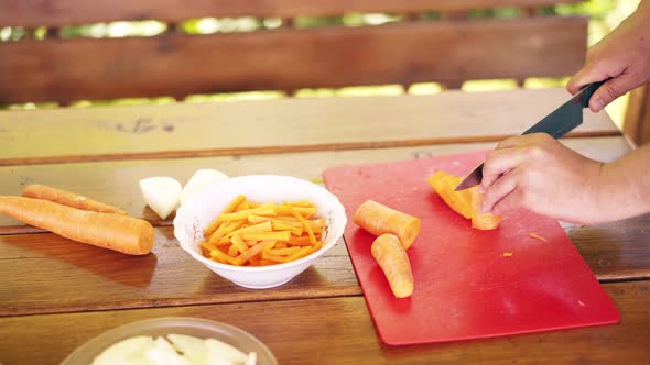 Closeup Guy is Cooking Pilaf It is in a Summer House Cuts Fresh Carrots on a Red Cutting Board