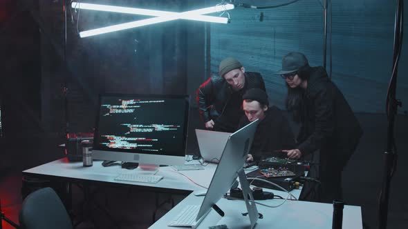 Three Hackers Talking and using Laptop in Dark Hideout