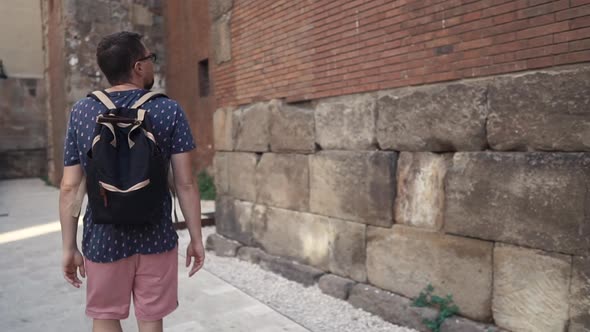 Young Man Is Walking Along Old Medieval Wall of Ancient Building in Summer Day
