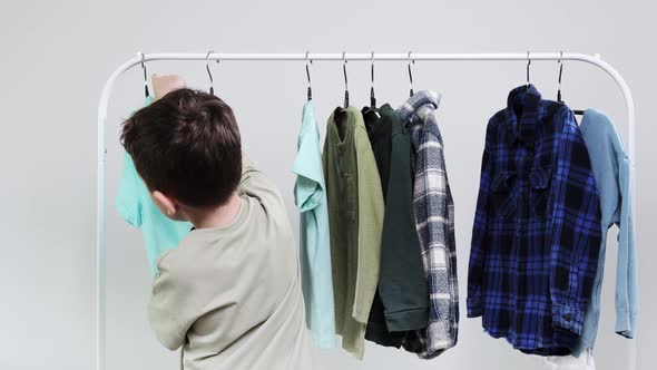 Boy preschooler standing by the hangers, racks up clothes, and chooses clothes for today.