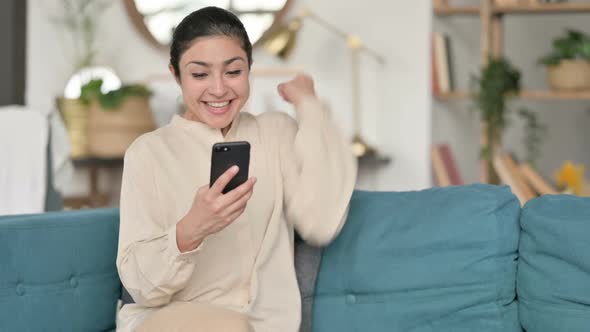 Indian Woman Celebrating Success on Smartphone on Sofa