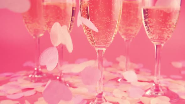 Falling confetti in the form of hearts on the background of glasses with sparkling wine