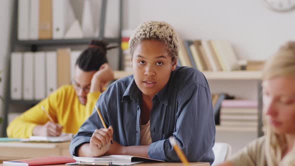 Cheerful Mixed-Race Female Student Taking Notes and Smiling at Camera