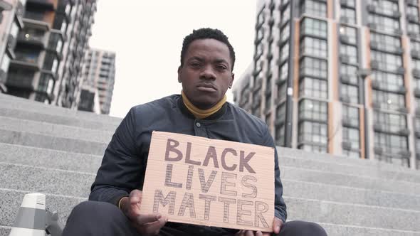 Closeup Man Sitting on the Stairs and Holding Carton Placard with Black Lives Matter Writing