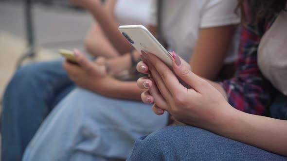 Closeup Hands of Teenage Girls Texting Fast on Smartphone Sitting on City Street Outdoors