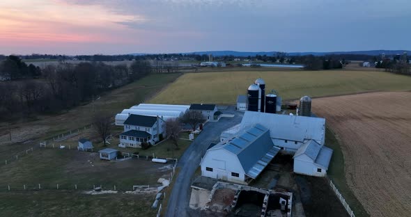American farm with barn buildings, silo, greenhouse in winter pasture setting. Aerial pullback revea