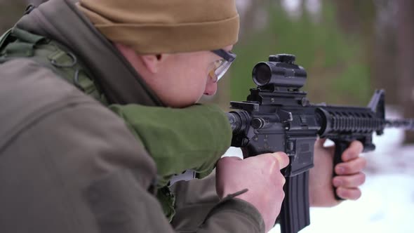 Shooting Over Shoulder of Male Soldier Aiming with Armed Gun Walking in Winter Forest