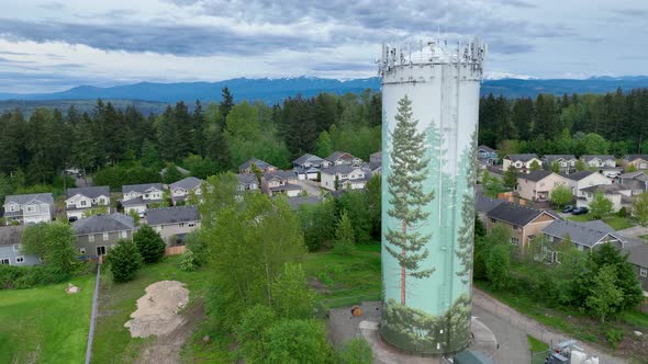 Drone shot of a suburban water tower with a large tree mural on the side of it.