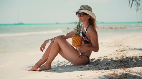 Tanned Girl In Bikini Sitting On Sand. Sexy Blonde Travel Girl Relaxing On Caribbean Beach.