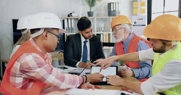 Construction Coworkers and their Successful Bearded Main Engineer Holding Joint Meeting