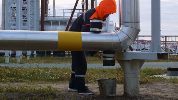 A Worker in the Oil and Gas Industry Brings a Bucket to the Pipeline Opens the Tap and Drains the