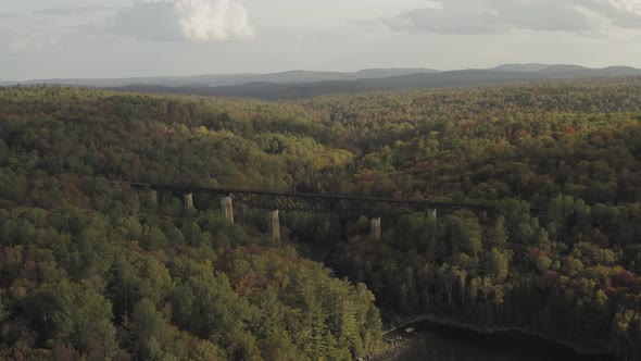 Railroad Trestle crossing the outlet of a lake with early fall foliage at sunset AERIAL PULL BACK