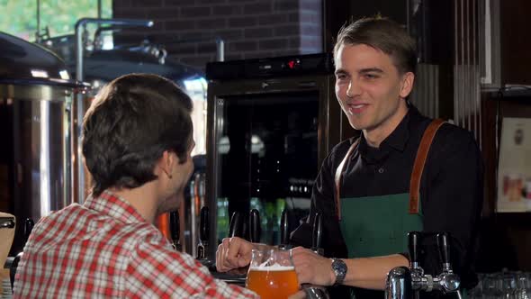 Happy Man Talking To a Bartender While Having Beer at Local Pub