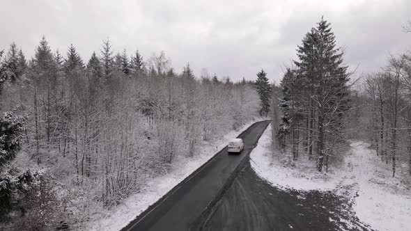 Van driving along an isolated road through a stunning, snow covered forest in the rural countryside