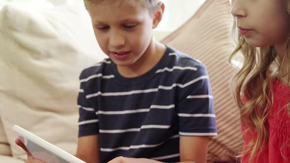 Siblings using digital tablet in living room