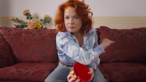 Angry Dissatisfied Retro Woman Throwing Popcorn Sitting on Couch at Home Looking at Camera