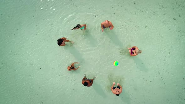 Aerial view of group of friends in swimwear playing volleyball in sea near beach.