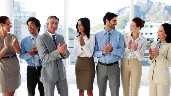Business team standing in a row clapping at camera