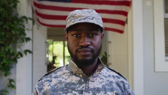 Portrait of african american male soldier standing in front of house and american flag