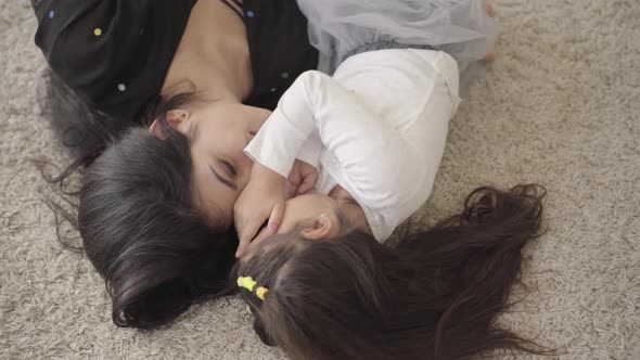 Close-up of a Smiling Middle Eastern Young Woman Laying with Her Cute Daughter at the Soft Carpet