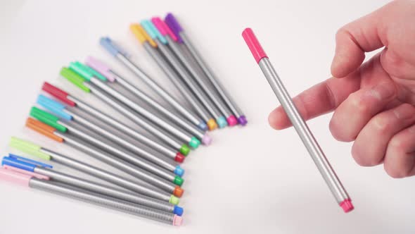 Gray pen with a red cap balances on a finger over a white table with multi-colored school supplies