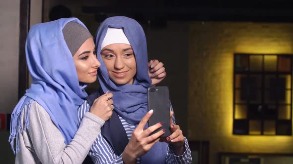 Modern Muslim Women Take Pictures on a Mobile Phone. Girls in Hijabs Talking and Smiling