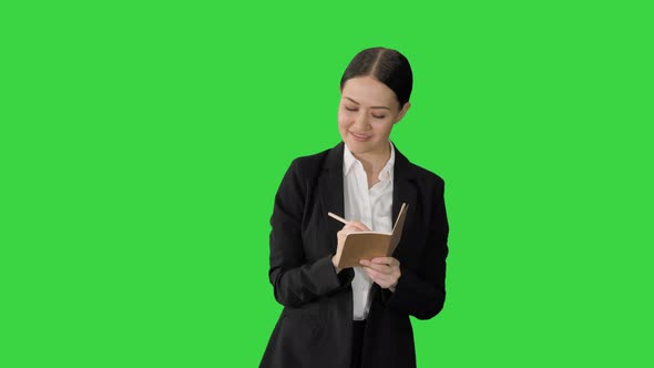 Concentrated Woman in a Suit Writing Business Ideas in Her Notepad While Walking on a Green Screen