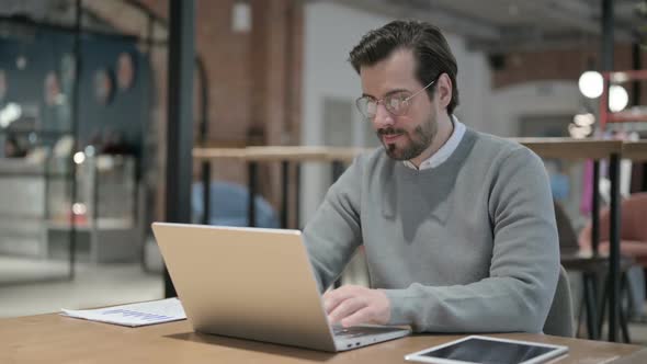 Young Man Coughing While Using Laptop in Office